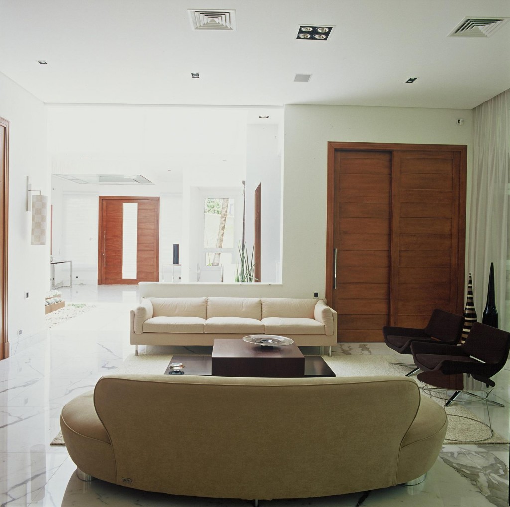 Com piso calaccata bianco e paredes claras, o living integrado com o hall de entrada banhado de luz natural graças a abertura zenital ficou mais amplo e destaca as portas em madeira.