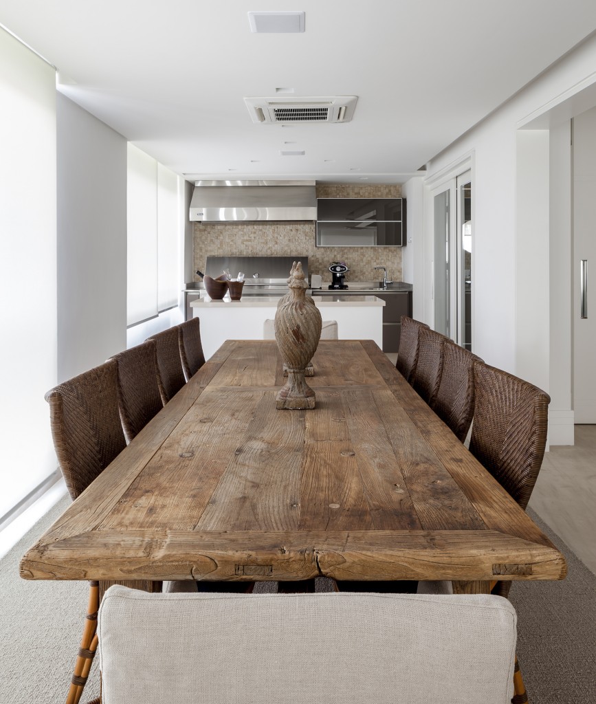 Integrada com o espaço gourmet, a sala de jantar tem mesa de demolição da Artefacto Beach & Country com cadeiras nas cabeceiras com capas em linho fendi e barrado também em linho marinho, e nas laterais cadeiras em málaca. Ao fundo, a bancada em Ilha de Tecnostone divide os dois espaços. Na parede Mosaicos da Mosarte e churrasqueira da Viking.